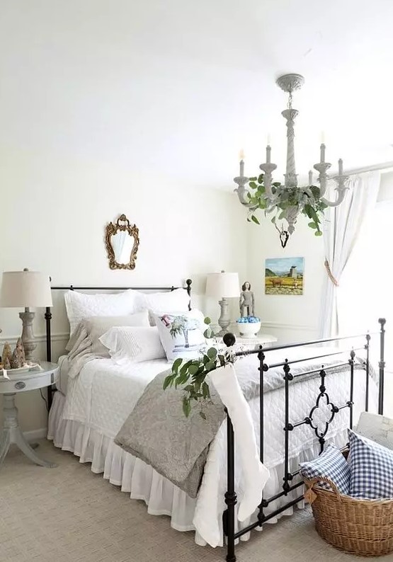 a beautiful rustic chic bedroom with a metal bed with neutral bedding, white and grey nightstands, greenery, a basket with pillows and a mirror in a chic frame
