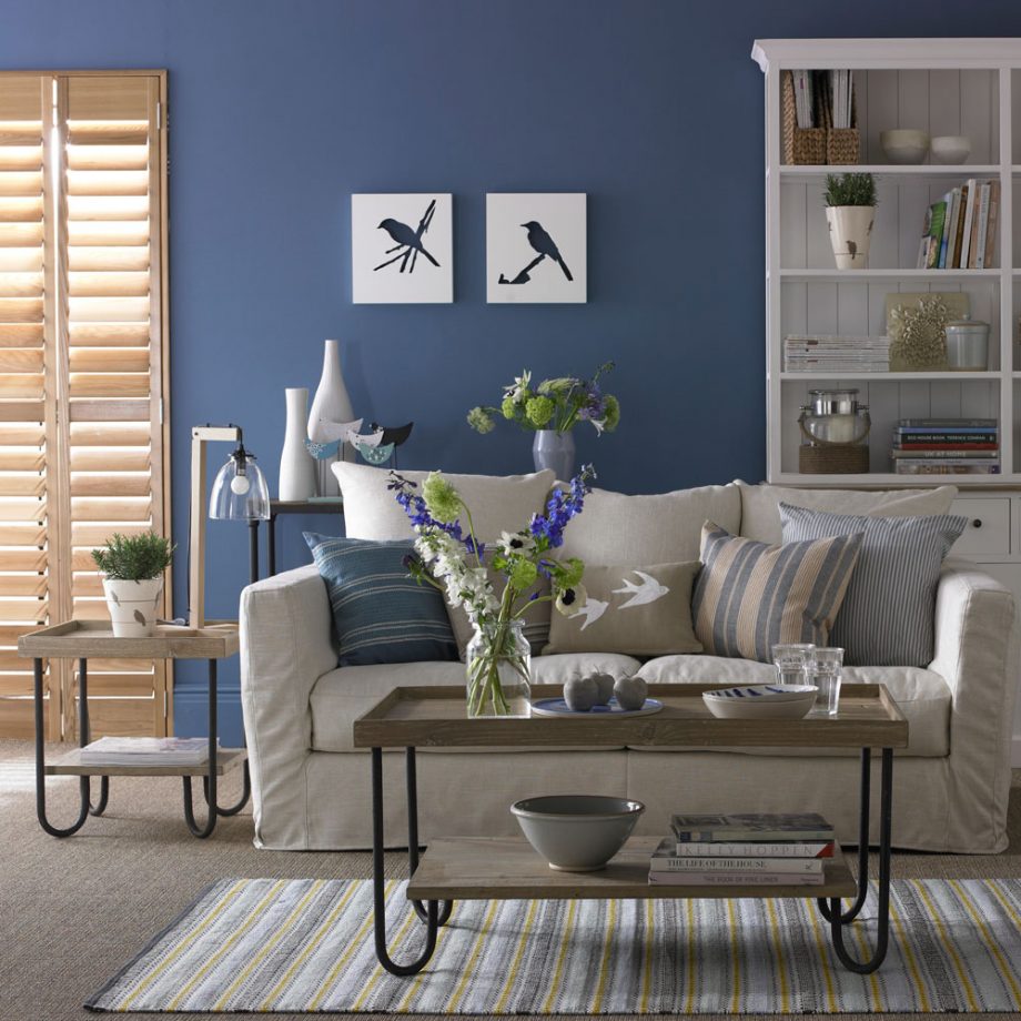 a blue living room with neutral furniture, striped textiles, hairpin leg tables, stripped back wooden shutters that add a soft natural touch