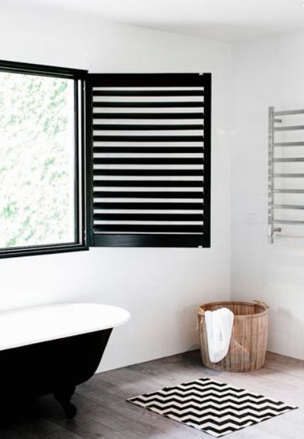 a modern farmhouse bathroom with black shutters, a black clawfoot bathtub, a printed rug, a basket with towels
