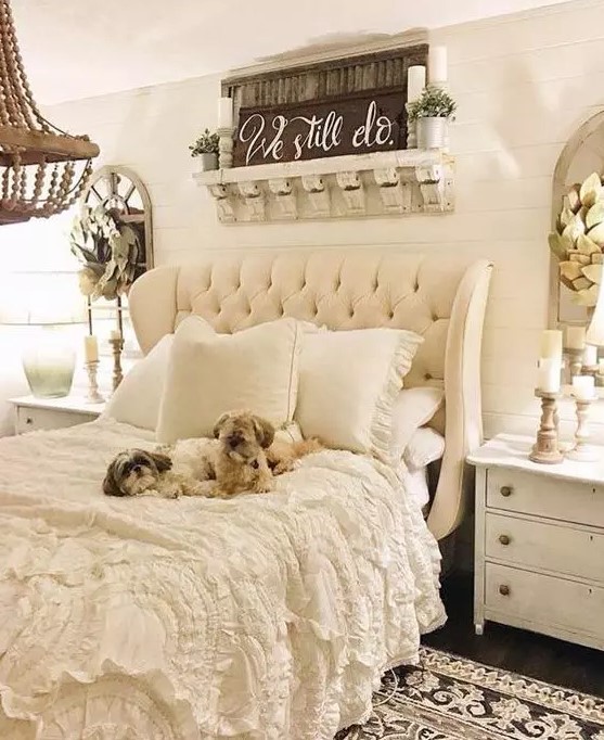 a neutral vintage and rustic bedroom with a shiplap wall, an upholstered bed, chic lace bedding, white nightstands, a wooden bead chandelier and candleholders