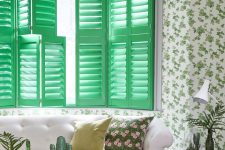 a pretty living room with botanical wallpaper, bright green shutters that add color and interest to the room, a white sofa and printed pillows, some cool green decor