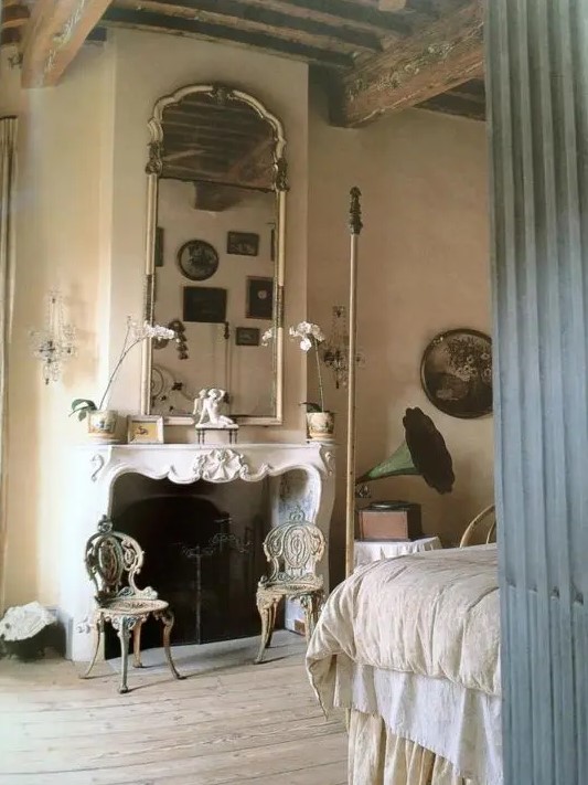 a refined French countryside bedroom with plaster walls, an antique fireplace, a large mirror, a bed with a canopy, chic carved chairs and vintage decor
