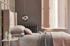 a relaxing and soothing bedroom with taupe walls, a pink upholstered bed with pastel bedding, a pendant lamp and blush solid shutters that match the color of the bed