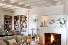 a romantic and neutral living room with a fireplace, neutral furniture and a trestle table, candleholders and a mirror on the mantel