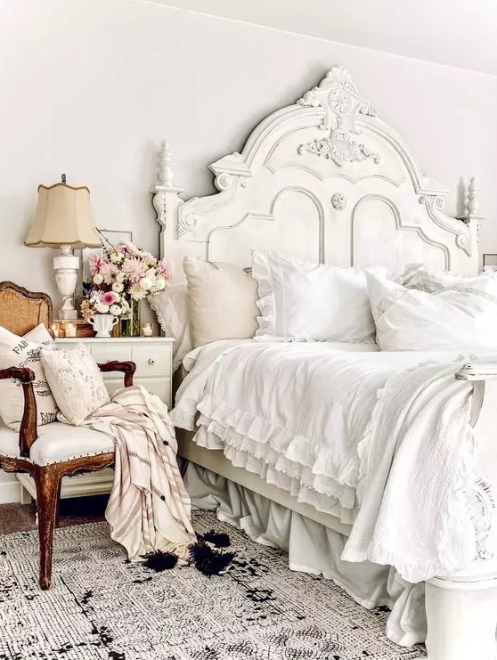 a sophisticated neutral French chic bedroom with a refined bed and bedding, a dresser, a chic creamy chair, a lovely lamp and some blooms