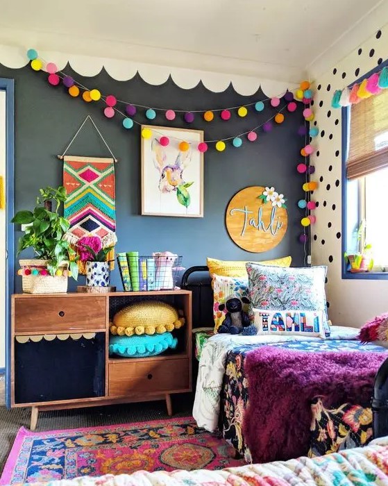 a bright kid's room with a black wall, colorful pompom garlands, pillows, bedding and a rug is extra bold