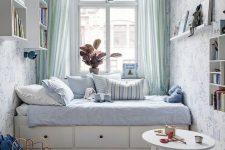 05 a delicate pastel kid’s space with blue wallpaper walls, a neutral bed with blue bedding, a round table, bookshelves and toys