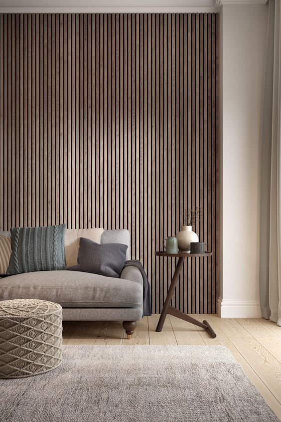a contemporary living room with a wood slat accent wall, a taupe sofa and a textural pouf, a side table