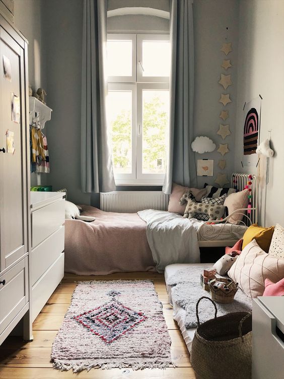 a neutral small kid's bedroom with a metal bed with pastel bedding, a sofa with pillows, a white dresser and a wardrobe