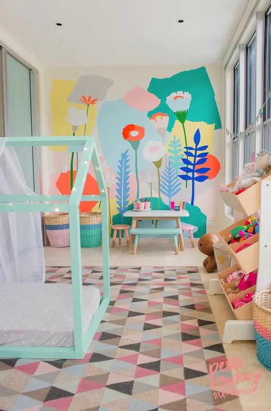 a pastel kid's room with a bright floral wall, a mint house-shaped bed, colorful toys and a bold rug and baskets