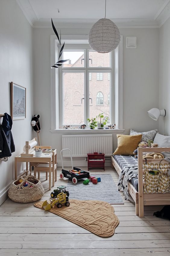 a Scandinavian kid's room with a stained bed and printed bedding, a stained desk and chair, baskets and a pendant lamp