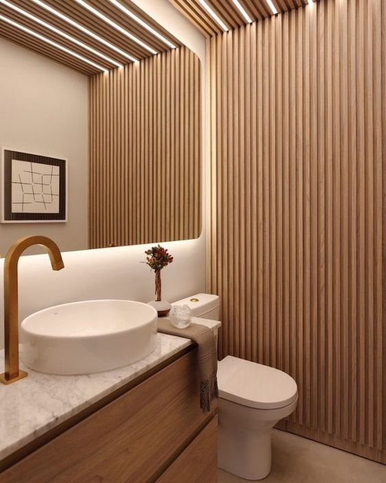 a contemporary neutral bathroom with a wood slat accent wall, a floating vanity, a white sink and a toilet and built-in lights