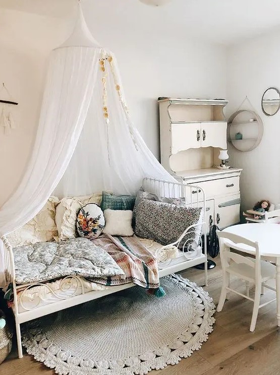 a shabby chic meets boho kid's room with neutral walls, white vintage furniture, pretty bright bedding and pillows and a canopy over the bed