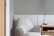 15 a contemporary space with a whitewashed wood slat accent wall, upholstered panels, a neutral chair with a footrest and a light-stained side table