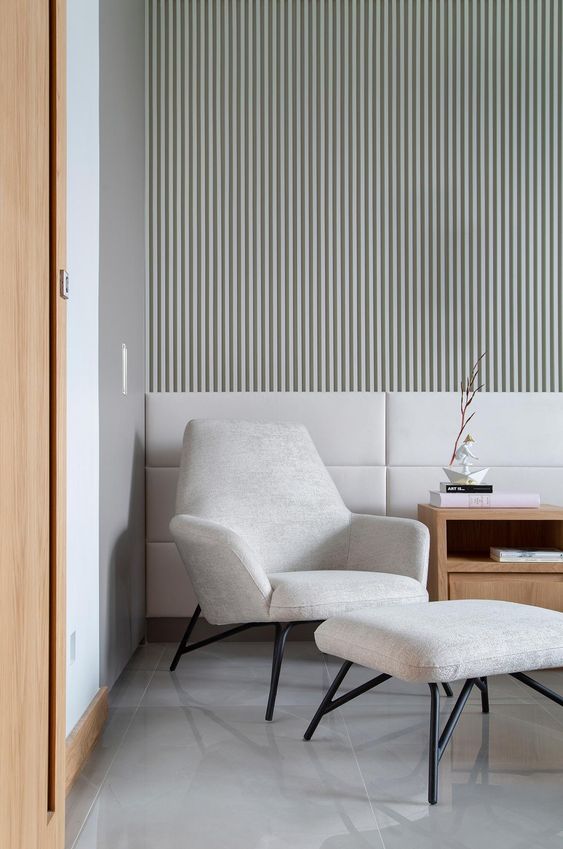 a contemporary space with a whitewashed wood slat accent wall, upholstered panels, a neutral chair with a footrest and a light-stained side table