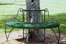 15 a refined curved bench of metal covering the tree partly is a chic and beautiful seat fr your garden, a green cushions makes sitting more comfortable