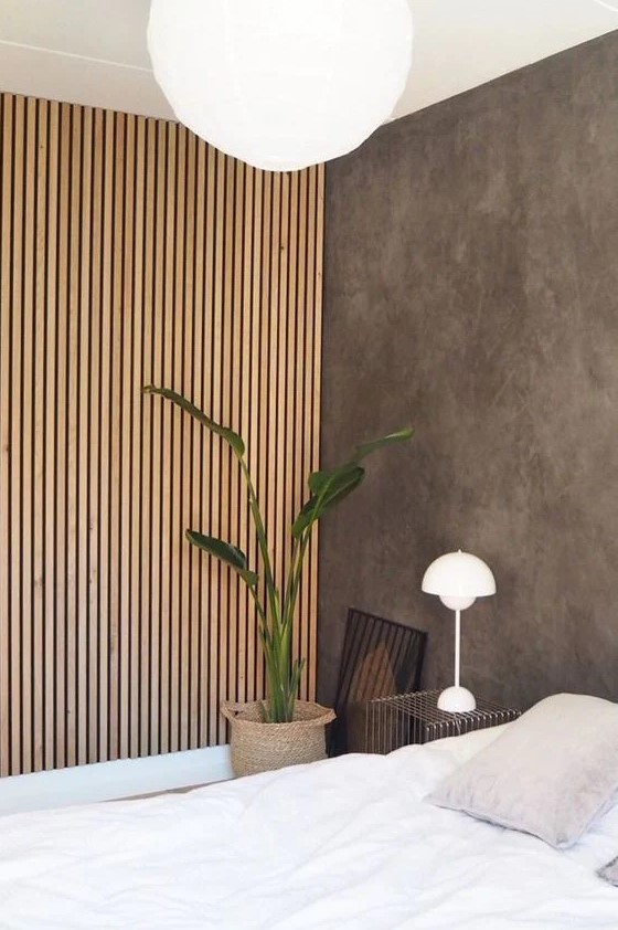 a minimalist bedroom with a concrete wall and a wood slat accent wall that hides a built-in wardrobe and adds coziness to the space