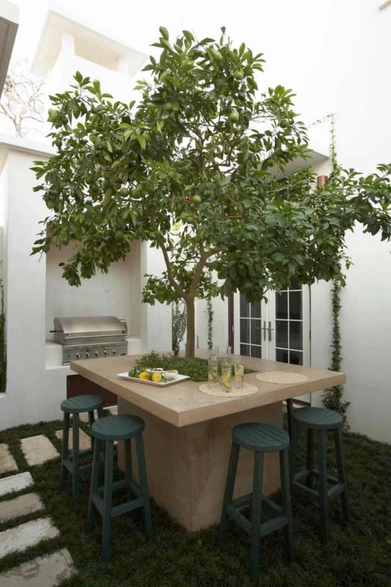 a small modern backyard showing off a living tree and a wooden table around it, navy stools around the table