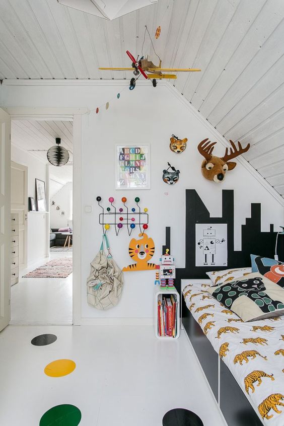 a small kid's room with a black bed with colorful bedding, a gallery wall, a colorful polka dot floor and a plane