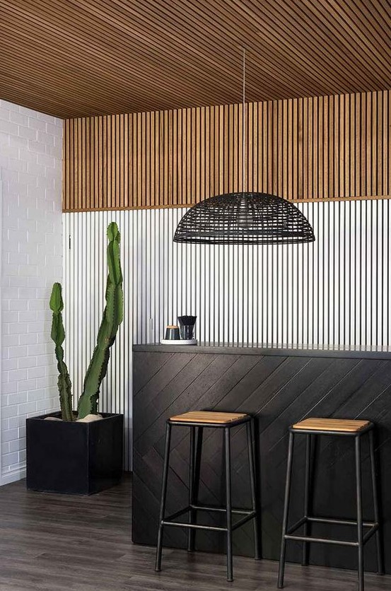 a minimalist kitchen with a black bar stand, with a wooden slat ceiling and accent wall with color blocking, a potted cactus and a black woven pendant lamp