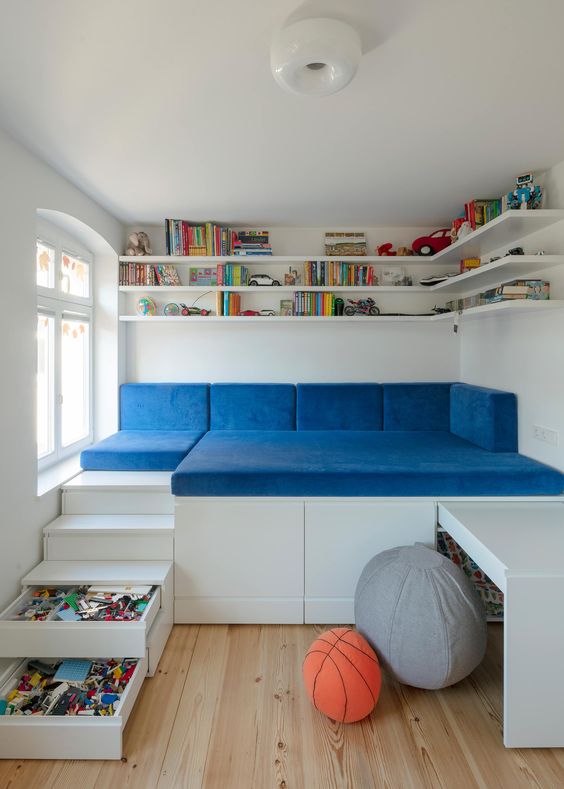 a small kid's space with open shelves, a raised sofa to sleep on, storage drawers and a built-in desk and bright touches