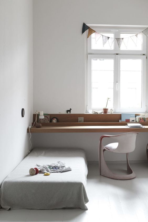 a small minimalist kids' room with a windowsill desk, a small chair and a low bed, a banner on the window and some lamps