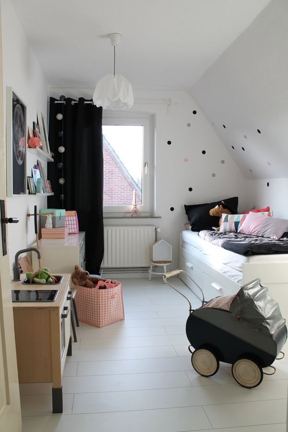 a small Nordic kids' room with a comfy storage bed, a white dresser, a black curtain, a play kitchen and some colorful touches