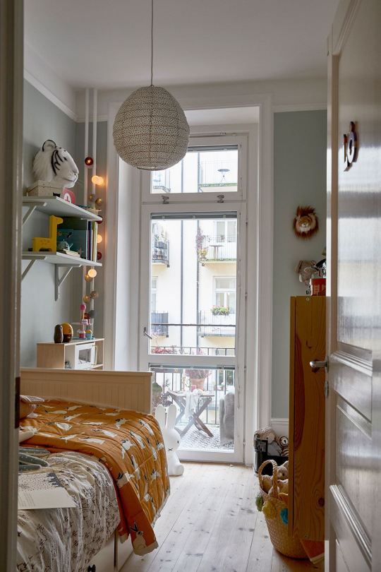 a small Nordic kid's space with grey walls, a white bed with printed bedding, a stained dresser, wall-mounted shelves and a pendant lamp