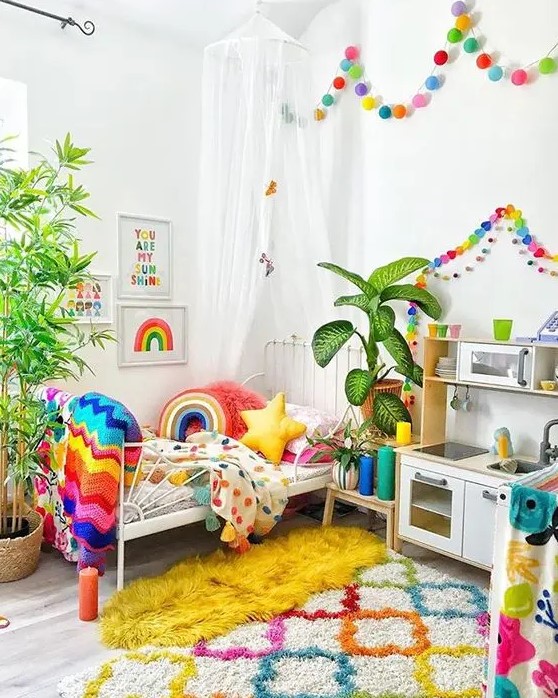 a super bold kid's room with rainbow color garlands, matching bedding, blankets and pillows, a colorful rug and artworks