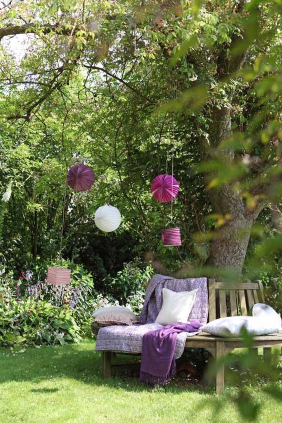a wooden bench wrapping the tree, with purple blankets, cushions and pillows, paper pompoms and hanging lanterns