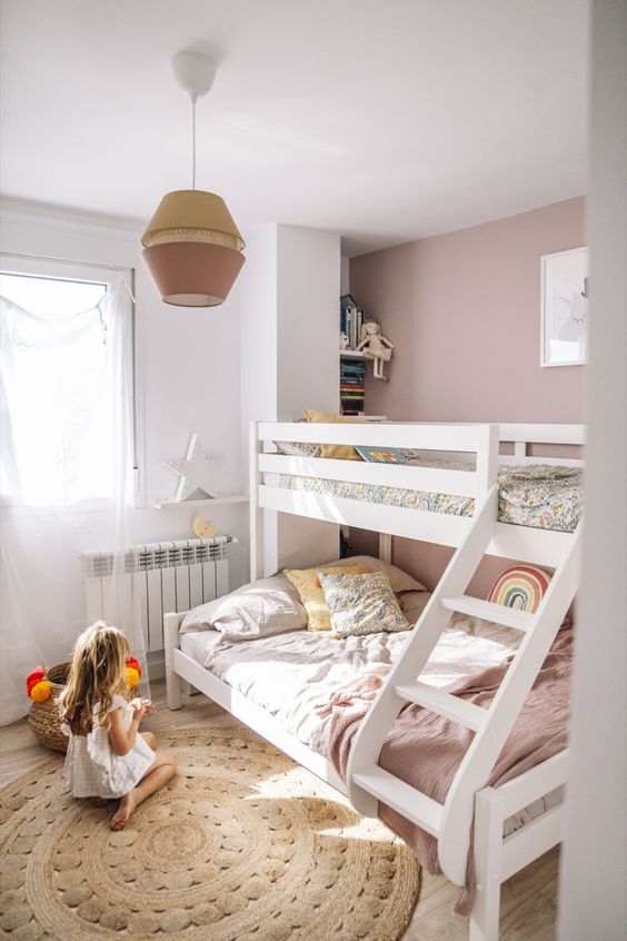 a beautiful mauve kids' bedroom with a bunk bed, a jute rug, a storage unit and open shelves plus a two-tone lamp