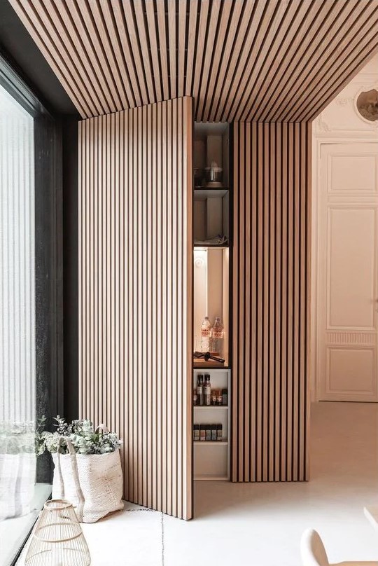 a neutral space with a wooden slat accent wall that extends to the ceiling and hides a pantry is a very smart and stylish solution for a kitchen