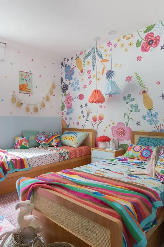 a colorful twin kid's room with a floral statement wall, colorful bedding and pillows, pendant lamps and a tassel garland