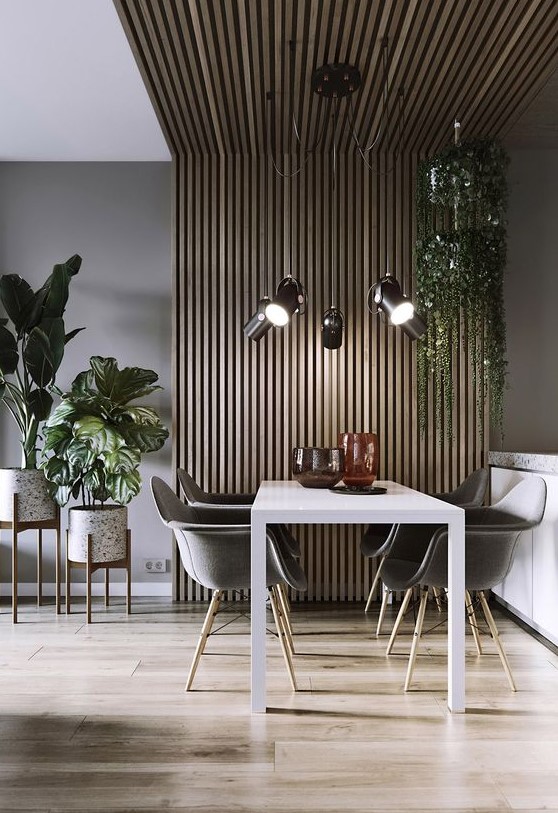 a lovely mid-century modern dining space with a wood slat accent wall and ceiling, a white table, grey chairs and lots of plants