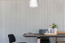 30 a mid-century modern dining room with a stained and whitewashed wood slat wall, a black table and black and stained chairs, a pendant lamp
