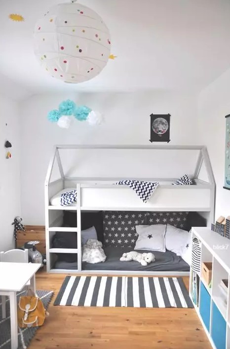 a Scandi kids' room with a bunk bed, printed bedding, a striped rug, a white table and chair, a white storage unit