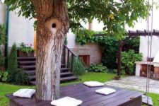 32 a dark deck around the tree with white pillows under the tree is a lovely space that welcomes you to the garden