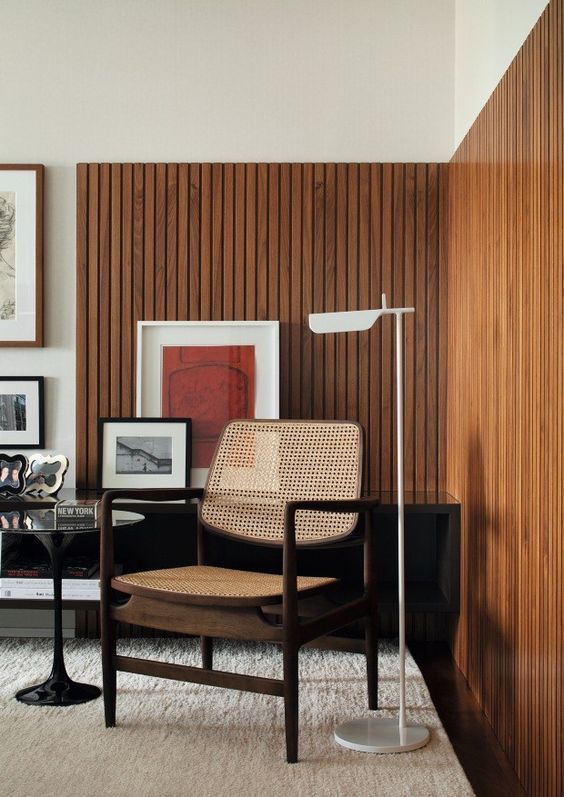 a mid-century modern living room with stained wood slat accent walls, a rattan chair, a black table and bright artwork