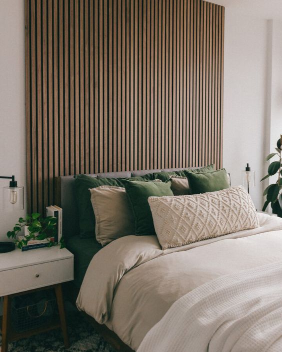a mid-century modern meets Scandinavian bedroom with a wood slat accent wall, a grey upholstered bed with neutral bedding, white nightstands and lots of potted plants