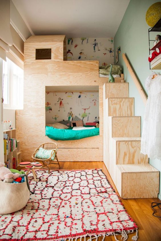 a small shared kids' space with a plywood bunk bed with colorful bedding, a printed rug, a bookshelf and a basket with toys