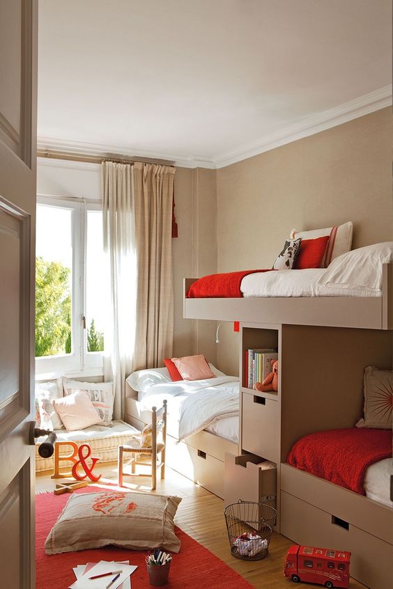 a small shared kids' space with taupe walls and three beds with storage, a sofa at the window and lots of pillows
