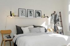 a Nordic bedroom with a neutral bed with neutral bedding, a black ladder as a storage unit, a black and white gallery wall