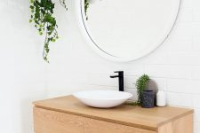 a Scandinavian bathroom done with white brick and terrazzo, a light-stained timber vanity, a round mirror and a bowl sink