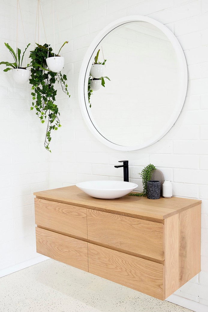 a Scandinavian bathroom done with white brick and terrazzo, a light-stained timber vanity, a round mirror and a bowl sink