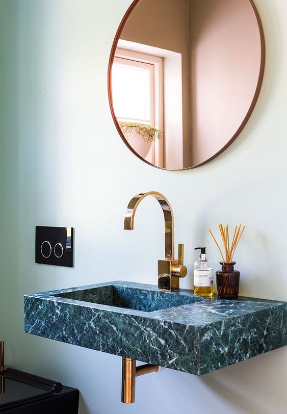 a beautiful contemporary bathroom with light green walls, a copper round mirror, a grene marble floating sink is a beautiful and chic space