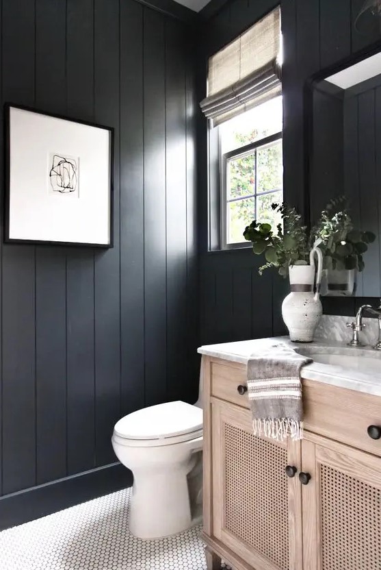 a black bathroom with beadboard walls, a white scale tile floor and a wooden vanity is a very cozy and welcoming space
