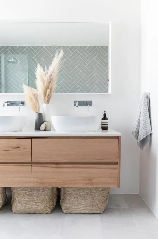a boho bathroom with a sleek wooden floating vanity, baskets for storage, a long mirror and pampas grass in vases