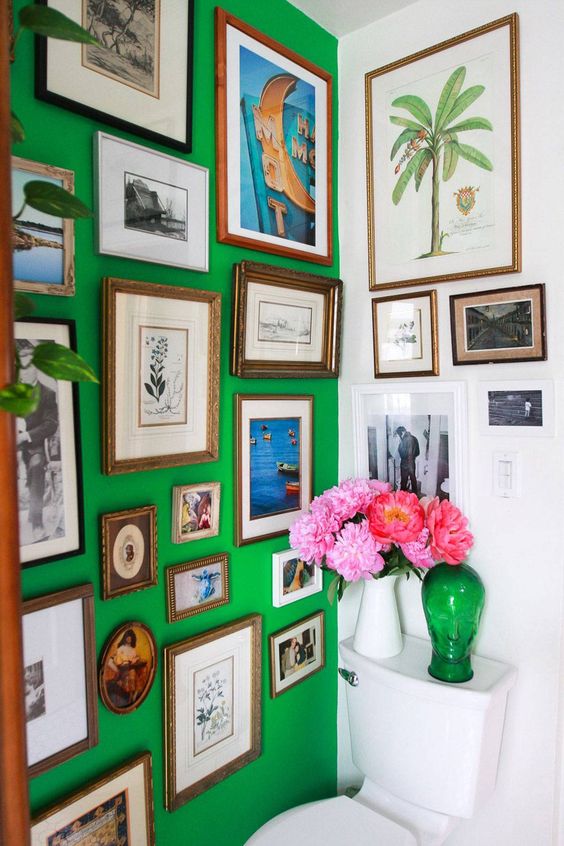 a bold and catchy bathroom with a green accent wall, a colorful gallery wall, white appliances and bold blooms