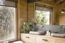a cabin bathroom of wood and concrete, with stone sinks, a large mirror and a large window for a view