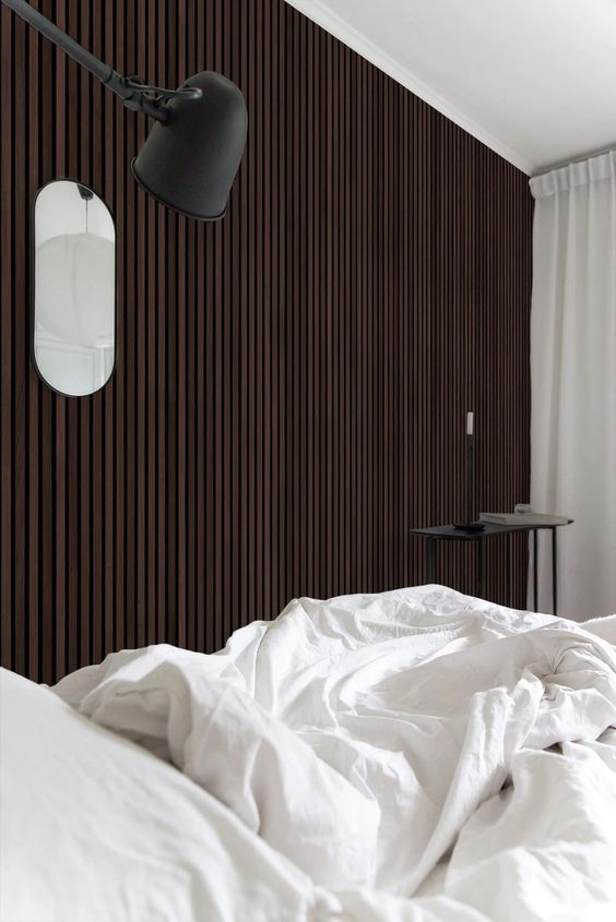 a catchy bedroom with a dark-stained wood slat accent wall, a bed with neutral bedding, a black coffee table and a black sconce